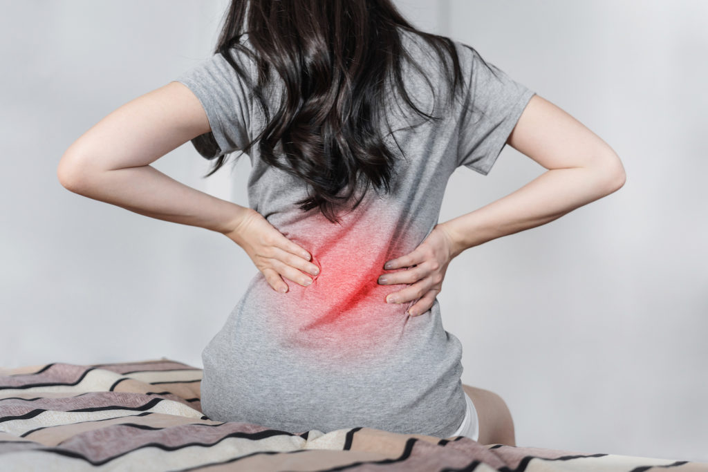 asian girl sitting on bed holding her hip pain